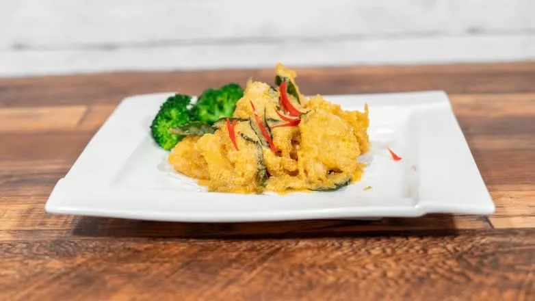Golden-sauced entrée with broccoli, served on a rectangular white plate