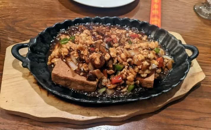 A sizzling platter with sauce and garnishes at Malay Morristown